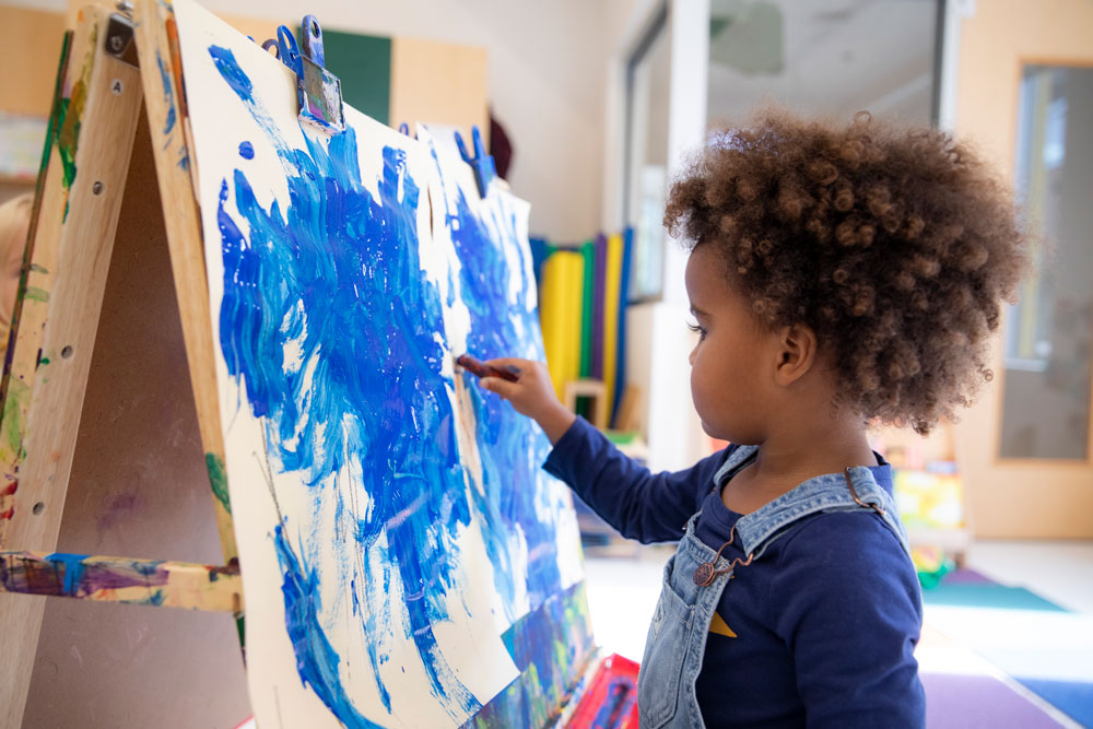 A child painting blue on a canvas at the New E3 School.